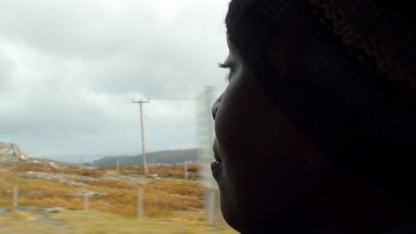 A woman looks out the window towards a dry orange landscape.