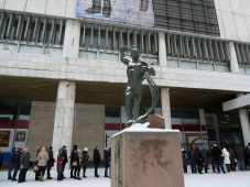 Bronze worker statues stands above a queue of people in the snow