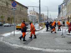 Team of snow shovellers in orange on city street with large buildings