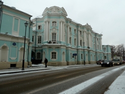Snow covered street and sidewalk with pedestrian before pastel blue and white Art Nouveau building