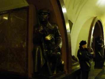 A soldier stands beside a USSR era bronze sculpture of a soldier kneeling beside dog.